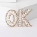 Macro detail of the OK shaped brooch featuring white pearls and colorful rhinestones - Gold