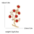 Goldene Pflaumenblüten-Brosche mit roten Perlen und weißen Strasssteinen auf Weiß - Rot