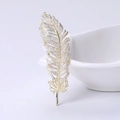 Elegant gold feather brooch with sparkling zircons displayed on a white ceramic bowl - Gold