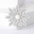 Macro detail of snowflake brooch with zircon crystal layers and center pearl on white steps - White