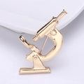 Macro shot of detailed gold metal microscope brooch with a polished finish on white base - Gold