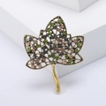 Vintage gold leaf brooch with colorful rhinestones on a minimalist white platform - Green