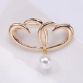 Dettaglio di una spilla a doppio cuore dorata con pendente di perla bianca su ceramica - Oro