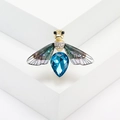 Macro shot of bee brooch featuring a large blue crystal and diamond-encrusted wings - Gold Purple