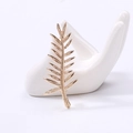 Dettaglio dell'elegante spilla a foglia dorata su un supporto a forma di mano in ceramica - Oro