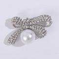 Detailed close-up of a silver bow brooch featuring sparkling rhinestones and a large pearl - Silver