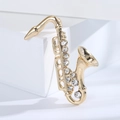 Detailed macro view of a golden saxophone brooch with sparkling rhinestones on a white base - Gold