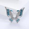 Macro detail of alloy butterfly brooch featuring blue gems, crystals, and a pearl center - Blue