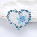 Dettaglio di spilla a cuore con perle, strass blu e decorazione floreale centrale - Blu