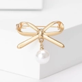 Vista dettagliata di una spilla a fiocco dorato con perla bianca su supporti geometrici - Oro