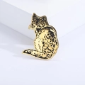 Dettaglio macro di spilla a gatto in acciaio dorato con texture spazzolata e macchie - Oro