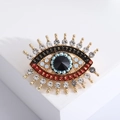 Detailed close-up of luxury evil eye brooch with blue beads and shiny crystal eyelashes - Gold