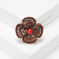 Close-up of vintage flower brooch with red pearls and gold-tone intricate hollow design - Red