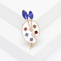 Artistic palette brooch with colorful rhinestones and paintbrushes on white podium - White