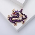 Spilla drago dorata con smalto viola e occhio di pietra rossa su sfondo bianco - Viola