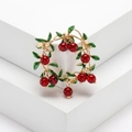Golden cherry wreath brooch with green enamel leaves and red beads on a white pedestal - Red