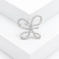 Elegant silver-toned bow brooch with rhinestones displayed on a white geometric stand - Bow / Silver