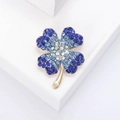 Eleganter goldener Kleeblatt-Anstecker mit blauem Strass-Verlauf auf weißer Plattform - Blau