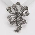 Elegant vintage silver ribbon bow brooch with black rhinestones on a white pedestal - Black