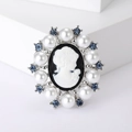 Vintage cameo brooch with white pearl border and blue rhinestones on white display - Silver