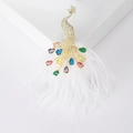 Detailed shot of gold peacock brooch with colorful crystals and white feather accents - White