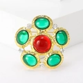 Vintage gold brooch with central red gemstone and surrounding green stones on white stand - Green And Red Glass White Rhinestone