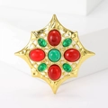 Makroaufnahme einer Goldstern-Brosche mit grünem Stein und roten Edelsteinen auf Weiß - Rot und Grün