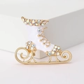 Detalle de broche de patín de hielo con esmalte y pedrería sobre un soporte minimalista - Blanco