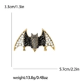 Spilla a forma di pipistrello in lega dorata con strass neri e bianchi su sfondo bianco - Nero