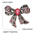 Vintage hollow bow brooch with pink rhinestones and a red pear-cut stone on white background - Pink