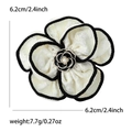 Detalle del broche de flor de camelia en tela crema con borde negro y centro de perla - Blanco