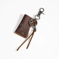 Detalle de funda de cuero para encendedor con mosquetón metálico y borlas de cuero - café