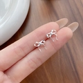 Elegant S925 sterling silver ribbon bow stud earrings shown on finger for size scale - 925 Silver / Silver (with Plastic Backings)