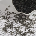 Macro shot of dark grey translucent glass seed beads in a white lace bowl for DIY crafts - 2mm / Black and Gray