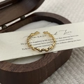 Detalle de un anillo ondulado dorado con circonitas sobre papel decorativo beige - Abierto Ajustable / Dorado