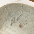 Detail eines runden rosa Kristallanhängers mit gezacktem Silberrand auf Keramik - 925er Silber / Erdbeerrot