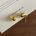Nahaufnahme polierter goldener Tropfenohrringe auf Vintage-Papier in minimalistischem Stil - 925er Silber / Gold