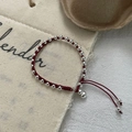 Detail eines roten geflochtenen Armbands mit Silberperlen und kleinem Glockenanhänger - Rotes Seil