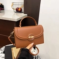 Brown litchi grain leather handbag with gold round buckle shown by a hand-held model - Brown