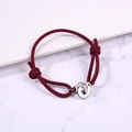 Detail of red braided rope bracelet with interlocking silver rings on marble surface - Burgundy