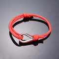 Red braided rope bracelet with a polished silver horseshoe buckle on black surface - Red