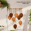 Detail eines Makramee-Wandbehangs mit erdfarbenen Blattmotiven an einer Holzstange - Brauner gewebter Wandteppich