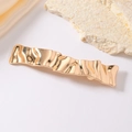 Elegant gold wavy metal hair clip with polished rippled texture on a minimalist background - Gold