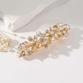 Detailed close-up of a gold floral hair clip with sparkling rhinestones on stone background - Gold