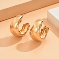 Primo piano di orecchini a cerchio a forma di C dorati lucidi su uno sfondo minimalista - Orecchini d'oro