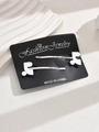 Detail of two silver metal hair clips with white enamel accents on black display card - White