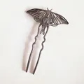 Macro shot of U-shaped metal hair fork featuring detailed hollow moth wing texture - Gunmetal