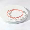 Pink wave-shaped fabric headband with white anti-slip comb teeth on a display stand - Orange