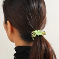 Detalle de una pinza para el cabello de tulipa verde en una coleta de mujer elegante - Flor de Ojo de Gato Verde