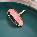Macro shot of a gold oval hair hook with pink marble texture on a green ceramic background - Pink